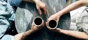 A man and a woman holding coffee cups as they have a conversation or hanging bridge above water